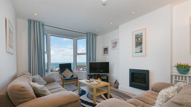 Una sala de estar con sofá, televisión, chimenea y vista al mar.