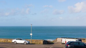 Un área de estacionamiento con vista al mar, un muro de piedra y un farol.