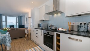 Una cocina moderna con armarios blancos, horno empotrado y microondas. Cuenta con una zona de comedor con mesa y sillas, y vistas al exterior a través de amplias ventanas.