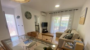 A living room with a glass-top coffee table, a sofa, a television, and a kitchen area in the background. - Daró 2D 167 - Community pool, corner house, A/C (Torroella de Montgri)