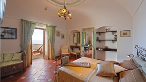A cozy room with a bed, a chair, a table, and a view of the sea through a window. - Casa Elena - In the center of Praiano, Parking & Panoramic Hot tub (Praiano)
