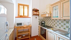 A compact kitchen with a microwave, toaster, coffee maker, and oven. There is a window with curtains, a spice rack, and a tiled backsplash. - Casa Elena - In the center of Praiano, Parking & Panoramic Hot tub (Praiano)