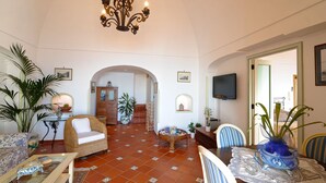 A spacious living area with a high ceiling, a chandelier, a television, and a dining table set with chairs. - Casa Elena - In the center of Praiano, Parking & Panoramic Hot tub (Praiano)