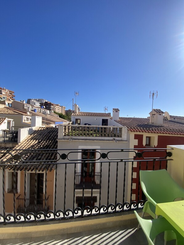 Un barrio residencial con tejados de tejas de arcilla, un balcón con barandilla metálica y un cielo azul despejado.