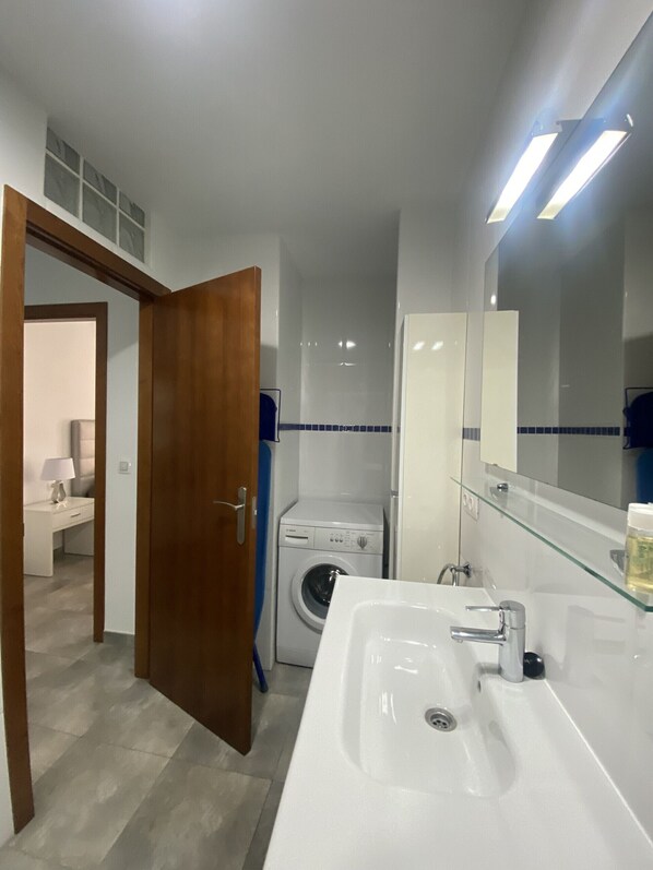 Un baño moderno con un espejo grande, lavamanos blanco y una lavadora.