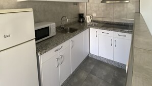 Una cocina compacta con gabinetes blancos, microondas, lavamanos y extractor de acero inoxidable.