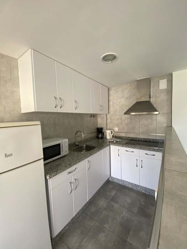 A compact kitchen with white cabinets, a microwave, a sink, and a stainless steel range hood.