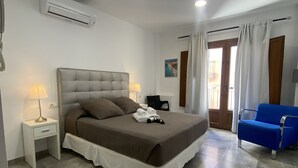 Un dormitorio con cama, mesitas de noche, una lámpara, un sillón azul y una puerta que da a un balcón.