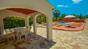 Ein überdachter Patio-Bereich mit Pool, Sitzgelegenheit im Freien und Blick ins Grüne.