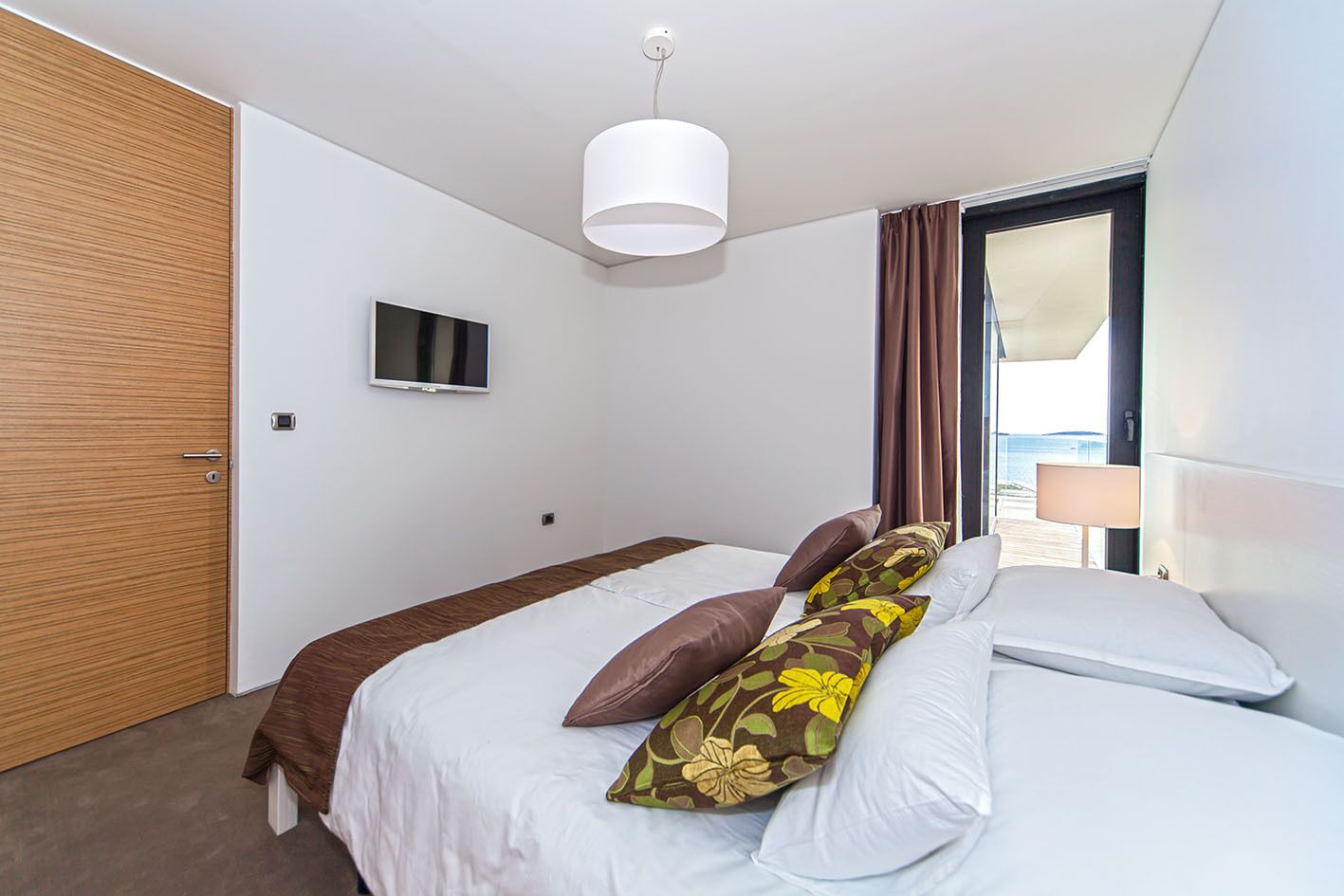 Habitación de hotel moderna con cama, televisión, ventana con cortinas y puerta.