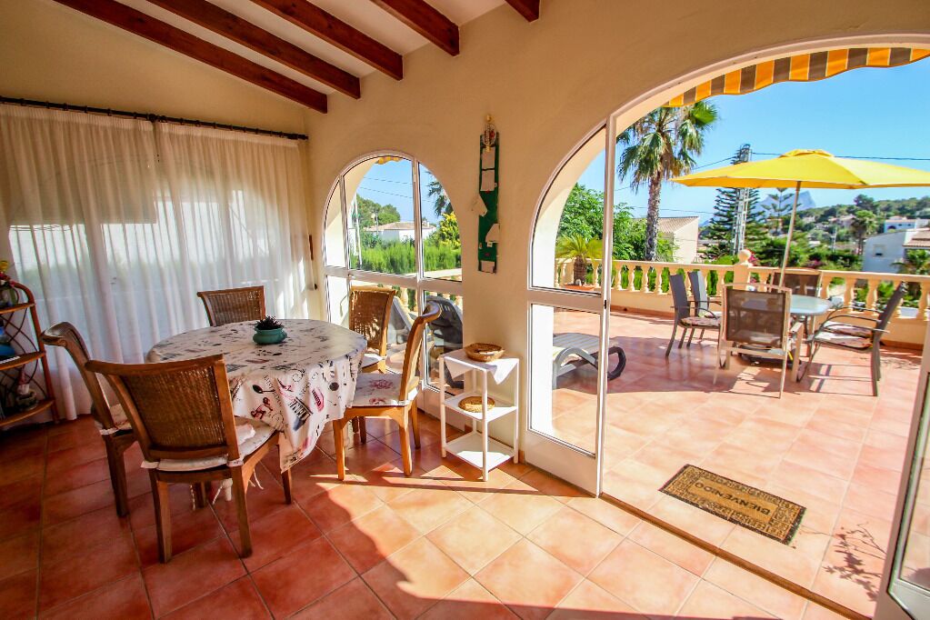 A sunlit patio with a round table and chairs, a yellow umbrella, and a view of the surrounding landscape.