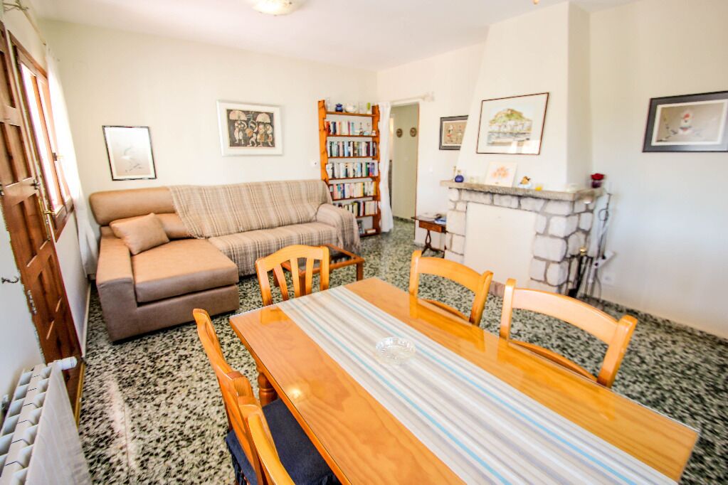 A cozy living room with a sofa, a dining table with chairs, a fireplace, and a bookshelf.