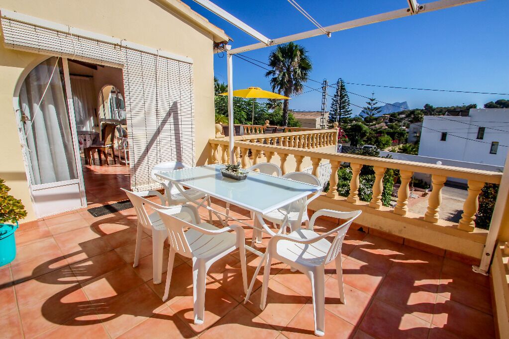 Un balcon avec une table et des chaises, un parasol jaune et une vue sur des immeubles et des arbres.
