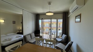 Een hotelkamer met een bed, een bank, een eettafel en stoelen. Er is een balkon met uitzicht op gebouwen.
