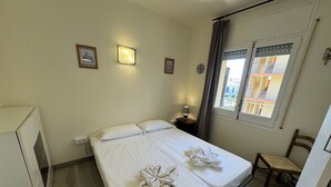 Hotelkamer met een bed, een stoel, een nachtkastje en een raam met uitzicht op gebouwen.