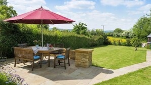 An outdoor patio with a table and chairs, a red umbrella, and a stone wall. - Swallows Rest Cottage - sleeps 6 guests  in 4 bedrooms (Broadway)