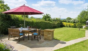 Un patio al aire libre con una mesa, sillas, un paraguas rojo y un muro de piedra.