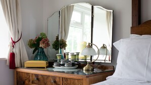 Une chambre à coucher avec une commode en bois, un miroir, une lampe de chevet et un vase rempli de fleurs.