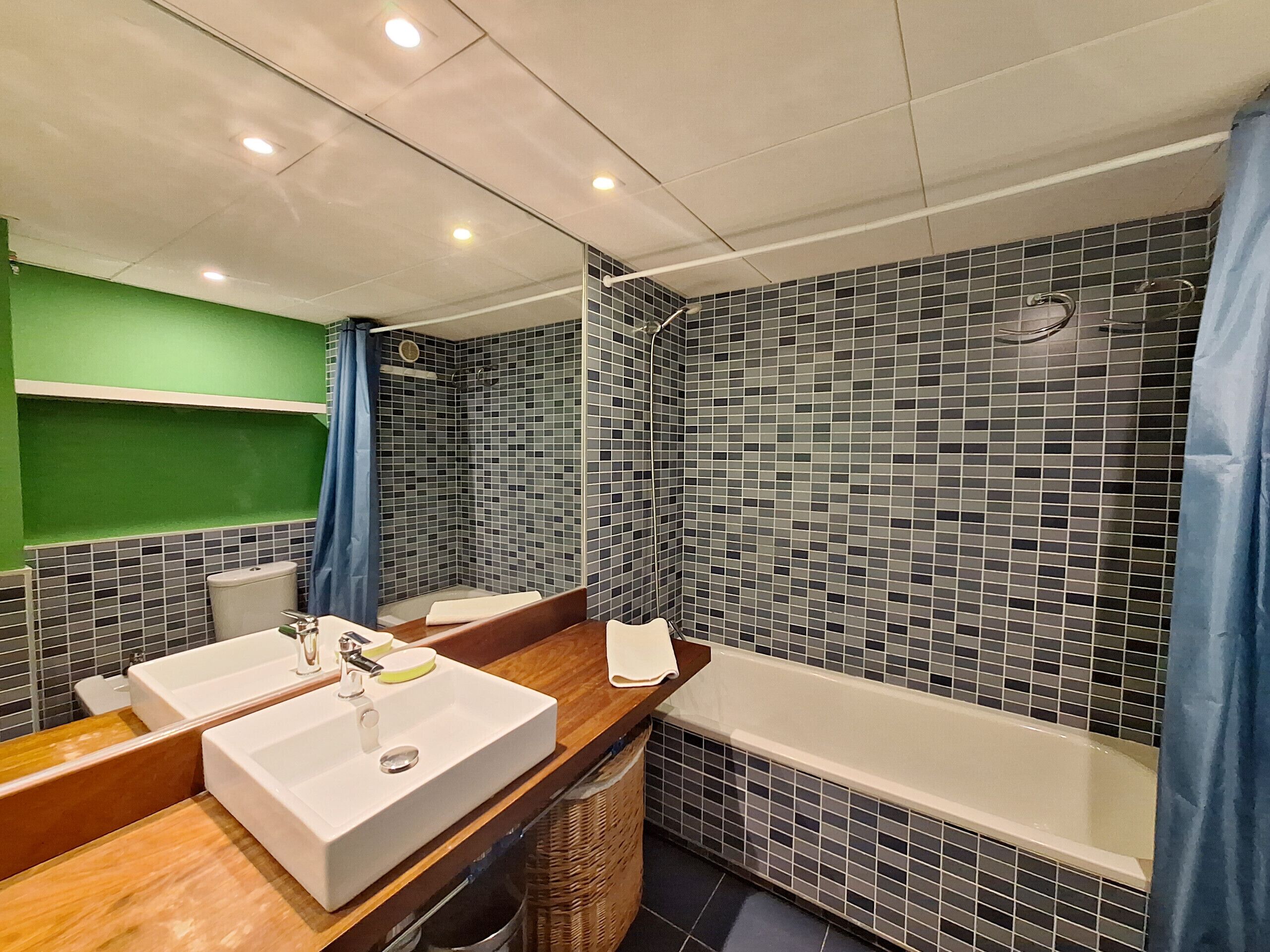 A modern bathroom with a large mirror, two sinks, a bathtub, and a shower with mosaic tiles.