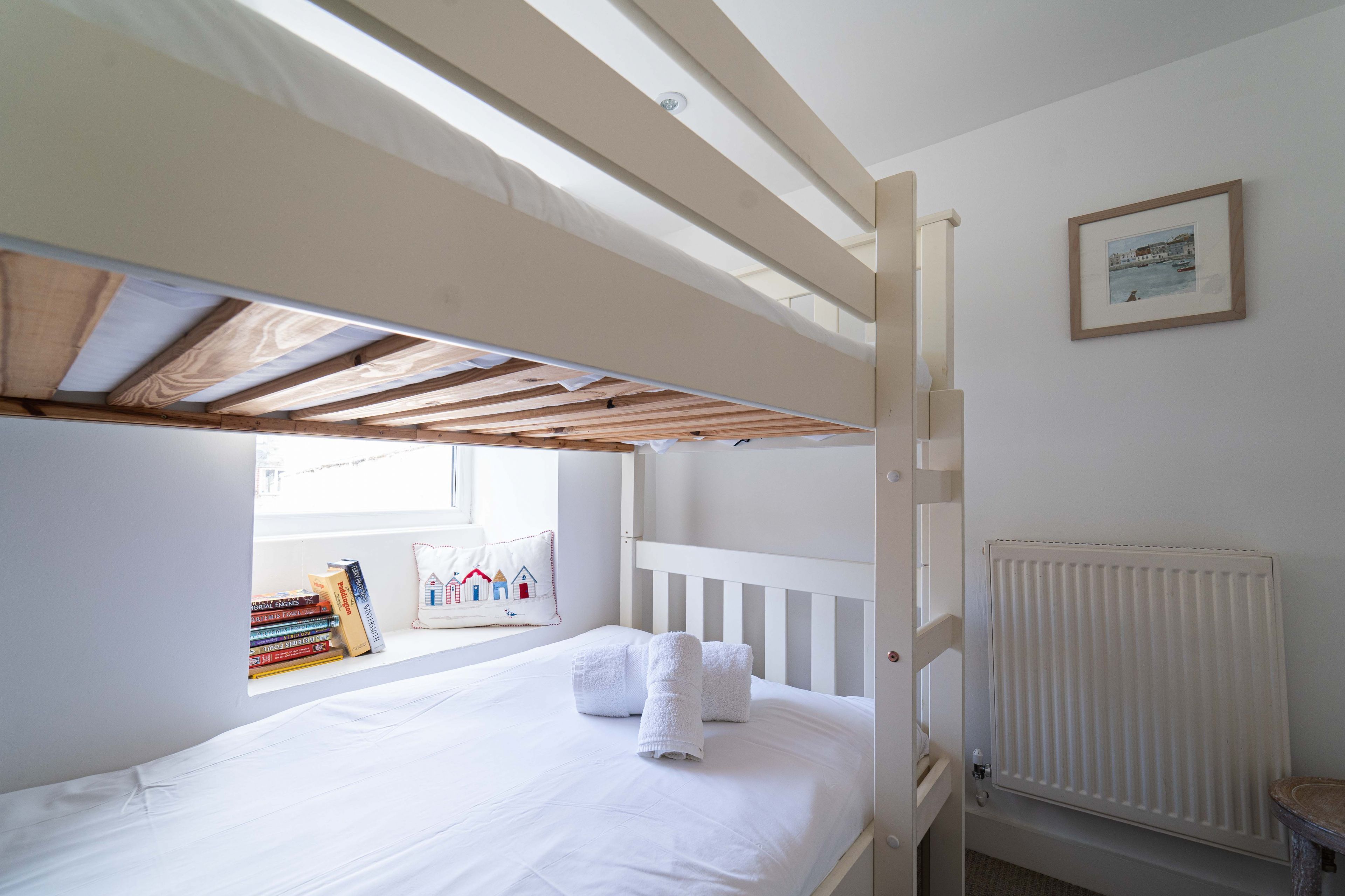 A bunk bed with a window, a radiator, and a framed picture on the wall.