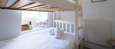 A bunk bed with a window, a radiator, and a framed picture on the wall.