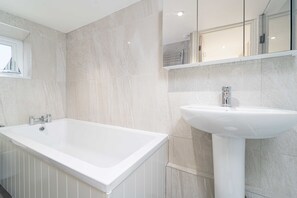 A modern bathroom with a large white bathtub, a pedestal sink, and a mirrored medicine cabinet.