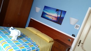 A hotel room with a bed, a wooden nightstand, a wall-mounted painting of a sunset, and a door. - B&B L'Isola (Porto Cesareo)