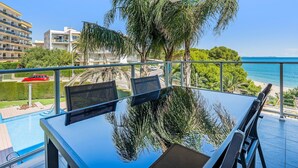 A balcony with a glass table and chairs, overlooking a pool and a beach. - Dream about front mediterranean sea views (Miami Platja)