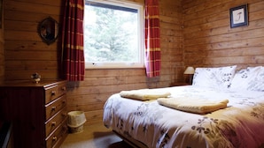 A wooden cabin bedroom with a bed, dresser, and window with curtains. - Steading Holidays - Strathconon (Acharacle)