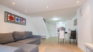 Ein modernes Wohnzimmer mit einem grauen Sofa, einem Essbereich mit weißer Möbel und einer Treppe, die in eine obere Ebene führt.