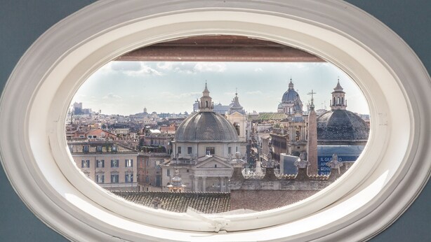 A view through a window of a cityscape with historical architecture, including domed buildings and a prominent church. - My Rome View Suite Apartment (Rome)