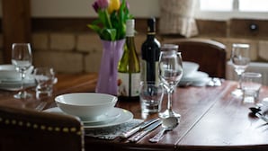 A dining table set with white plates, bowls, cutlery, and wine glasses, with a vase of flowers and bottles in the background. - A sudeley castle cottage that sleeps 4 guests  in 2 bedrooms (Cheltenham)