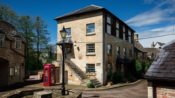 A traditional stone building with a staircase leading to the entrance, a red telephone booth, and a street lamp. - A sudeley castle cottage that sleeps 4 guests  in 2 bedrooms (Cheltenham)