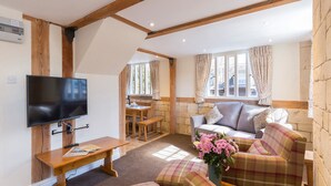 A cozy living room with a flat-screen TV, wooden furniture, a sofa, and a dining area with a table and chairs. - A sudeley castle cottage that sleeps 4 guests  in 3 bedrooms (Cheltenham)
