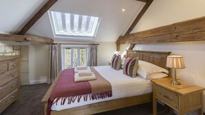 A bedroom with a skylight, wooden beams, a bed with pillows, a nightstand, and a dresser. - A sudeley castle cottage that sleeps 4 guests  in 3 bedrooms (Cheltenham)