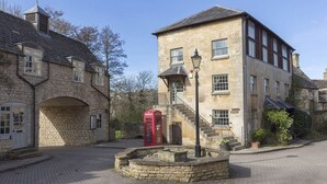 A stone building with a red telephone booth, a staircase, and a well-maintained courtyard. - A sudeley castle cottage that sleeps 4 guests  in 3 bedrooms (Cheltenham)
