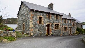 A stone house with a sloped roof, a chimney, and a small porch with potted plants. - Cottage 108 - Cleggan (Cleggan)