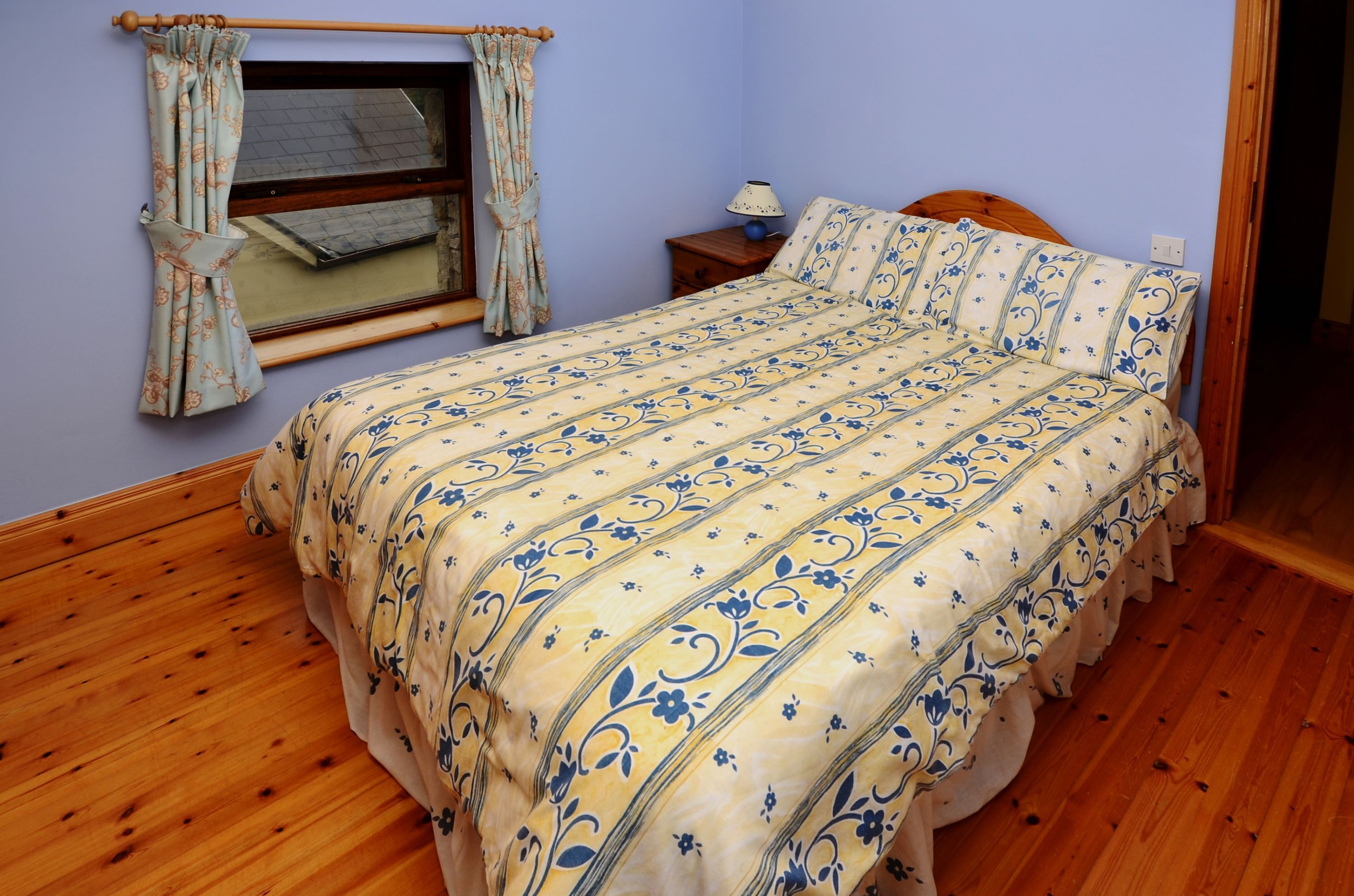 A bedroom with a wooden bed, a nightstand, a lamp, and a window with curtains.