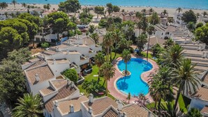 Et resort med swimmingpool omgivet af palmer og udsigt til stranden.