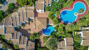 Oversigtsbillede af et resort med flere hytter, en central swimmingpool og grøn bevoksning omkring.