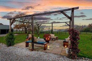 An outdoor patio with a wooden pergola, seating, and a fire feature.