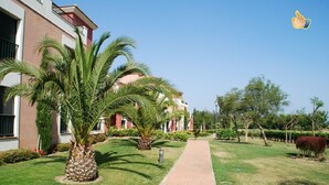 A pathway leading to a building with a red facade and palm trees. - Prado Golf - Isla Canela Golf GPHG77P68 (Isla Canela)