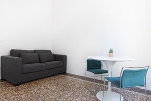 Una habitación moderna con un sofá gris, una mesa redonda blanca y sillas color turquesa.