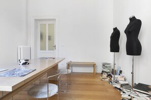 A minimalist room with a wooden table, two bar stools, a bench, and a wall-mounted radiator.