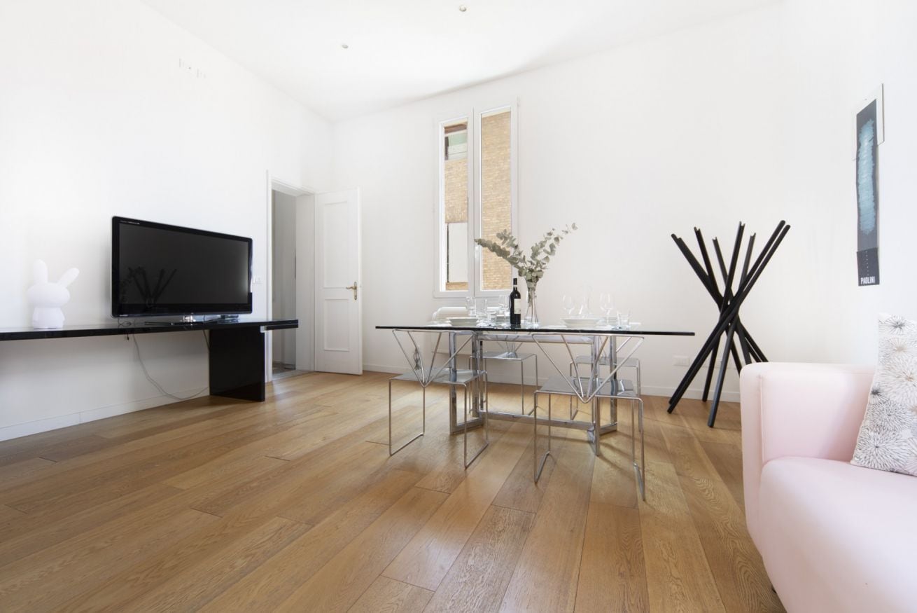 A modern living room with a glass dining table, a flat-screen TV on a black stand, and a pink sofa.