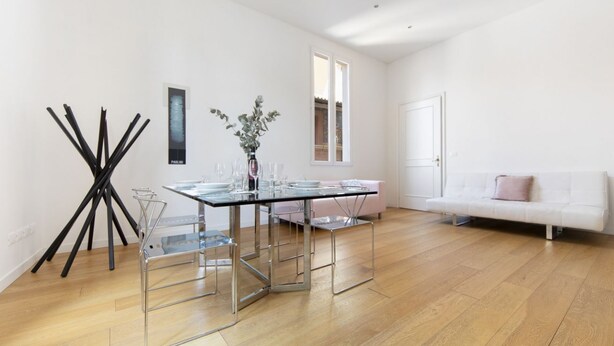 A modern living room with a glass dining table, clear chairs, a white sofa, and a large window. - UR-NEST Battisti 2 Deluxe (Bologna)
