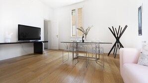 A modern living room with a glass dining table, a flat-screen TV on a black stand, and a pink sofa. - UR-NEST Battisti 2 Deluxe (Bologna)