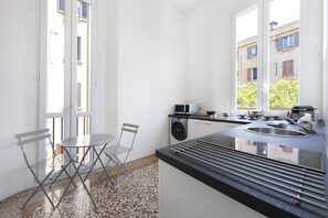 A compact kitchen with a dining area, a washing machine, and a window with a view of buildings. - UR-NEST Battisti 2 Deluxe (Bologna)