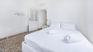 A hotel room with a neatly made bed, a white door, and a tiled floor. - UR-NEST Battisti 2 Deluxe (Bologna)