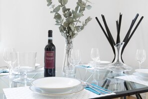 Mesa de comedor dispuesta con cristalería transparente, una botella de vino y un florero con hojas de eucalipto.